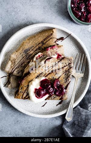 Toasty und nussige Buchweizencremes mit gerösteten Kirschen, Schlagsahne und bittersüßer Schokolade. Ein natürlich glutenfreies Dessert. Stockfoto