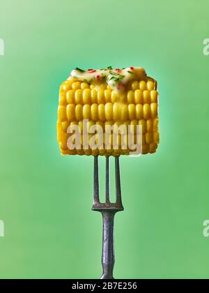 Mais auf dem Cob mit geschmolzener Butter, tropft auf einer Gabel, vor grünem Hintergrund Stockfoto