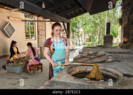 Usbekisches Mädchen, das die Maulbeerbaumbarken aus heißem Wasser in Konighil-Dorf in der Nähe von Samarkand nimmt, wo sie Seidenpapier auf traditionelle Weise herstellen. Stockfoto