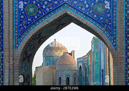 Blick über die Mausoleen und Kuppeln des historischen Friedhofs von Shahi Zinda durch ein bogenförmiges Tor, Samarkand, Usbekistan Stockfoto