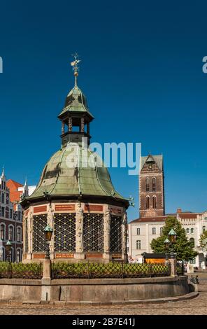 Stadtbrunnen am Marktplatz mit Maria-Turm in der Ferne in Wismar, Mecklenburg-Vorpommern, Deutschland Stockfoto