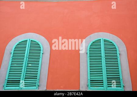 Zwei grüne Woddenfenster an einer orangefarbenen Wand in Italien Stockfoto