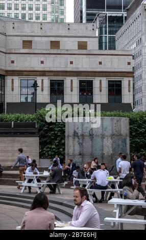 Büroangestellte in London essen an einem warmen Tag Mittagessen, Chat und Geselligkeit an externen Tischen am Cabot Square, Canary Wharf. Hohe Bürogebäude im Hintergrund. Stockfoto