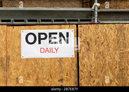 "Open daily" sign on scaffolding, chipboard background Stockfoto