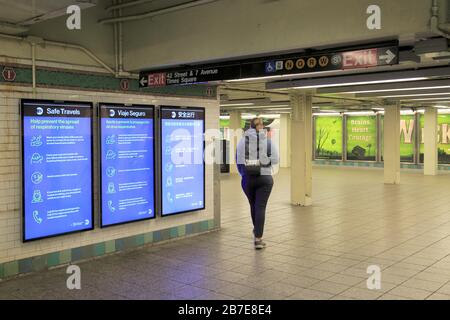 Woman spaziert durch MTA-Schilder mit Informationen darüber, wie man vermeidet, verhindert die Ausbreitung von Coronavirus in der leeren U-Bahn-Station Times Square, NYC, 15. März 2020 Stockfoto