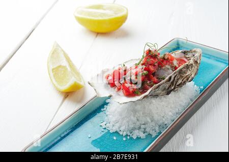 Frische Austern mit Tomaten und Kräutern auf dem blauen Teller, Tisch mit Austern, Zitrone und Salz. Tabellenansicht von oben. Gesunde Meeresnahrung. Frisches rohes Oyster-Dinner i Stockfoto