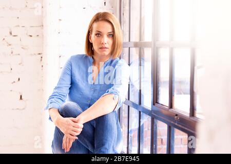Porträtaufnahme einer attraktiven Frau mittleren Alters, die sich am Fenster entspannt. Stockfoto