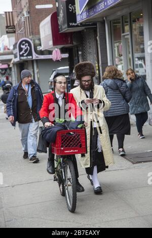 Die orthodoxe jüdische Gemeinde im Borough Park Brooklyn feiert den festlichen Urlaub von Purim, indem sie Kostüme trägt, Armen spendet, leckere Speisen isst und im Allgemeinen eine gute Zeit hat. Die Leute auf der 13th Avenue. Purim wird jedes Jahr am 14. Des hebräischen Monats Adar gefeiert. Es erinnert an die Errettung des jüdischen Volkes im alten Perserreich aus Hamans Handlung "alle Juden, jung und alt, Säuglinge und Frauen, an einem einzigen Tag zu vernichten, zu töten und zu vernichten", wie in der Megillah (Buch Esther) festgehalten. Stockfoto