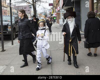 Die orthodoxe jüdische Gemeinde im Borough Park Brooklyn feiert den festlichen Urlaub von Purim, indem sie Kostüme trägt, Armen spendet, leckere Speisen isst und im Allgemeinen eine gute Zeit hat. Die Leute auf der 13th Avenue. Purim wird jedes Jahr am 14. Des hebräischen Monats Adar gefeiert. Es erinnert an die Errettung des jüdischen Volkes im alten Perserreich aus Hamans Handlung "alle Juden, jung und alt, Säuglinge und Frauen, an einem einzigen Tag zu vernichten, zu töten und zu vernichten", wie in der Megillah (Buch Esther) festgehalten. Stockfoto