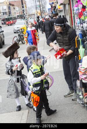 Die orthodoxe jüdische Gemeinde im Borough Park Brooklyn feiert den festlichen Urlaub von Purim, indem sie Kostüme trägt, Armen spendet, leckere Speisen isst und im Allgemeinen eine gute Zeit hat. Die Leute auf der 13th Avenue. Purim wird jedes Jahr am 14. Des hebräischen Monats Adar gefeiert. Es erinnert an die Errettung des jüdischen Volkes im alten Perserreich aus Hamans Handlung "alle Juden, jung und alt, Säuglinge und Frauen, an einem einzigen Tag zu vernichten, zu töten und zu vernichten", wie in der Megillah (Buch Esther) festgehalten. Der örtliche Händler gibt jüdischen Kindern Geschenke, wenn sie vorbeikommen. Stockfoto