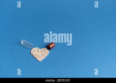 Granulat aus einer herzförmigen Kapsel auf klassischem blauem Grund gegossen. Herzförmige Medikamente. Herzsymbol durch Pillen gezeichnet. Stockfoto