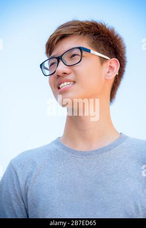 Low Angle Shot gutaussehender asiatischer Teenager mit Brille, Portrait fröhlicher Flusspferd junger Mann lächelt mit einem glücklichen Gesicht in Thailand Stockfoto