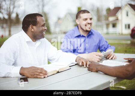 Eine Gruppe von verschiedenen Leuten, die am Tisch sitzen und lesen Die Bibel Stockfoto