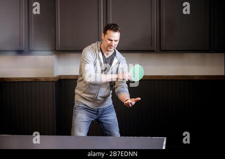 Junger kaukasischer Mann, der tagsüber Tischtennis spielt Stockfoto