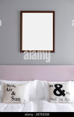 Bilderrahmen in einem minimalistischen Schlafzimmer im Grau- und Rosenthema hängen an der Wand über dem Bett. Stockfoto