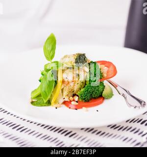 Gedämpftes Kabeljaufilet mit Brokkoli, Tomate, Zitrone, Avocado, Basilikumsoße und Pinienkerne auf weißem Grund. Kopierbereich Stockfoto