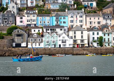 Altes blaues Boot, das Häuser am Hang bei Dartmouth, Devon, England passiert Stockfoto