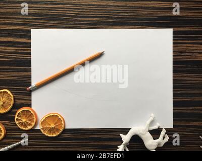 Weißes Papier zusammen mit einem Bleistift, Orangen und einem Hirschspielzeug auf eine Holzfläche legen Stockfoto