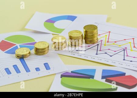 Vergrößern von Goldmünzenstapeln und farbigen Grafiken auf gelbem Hintergrund. Erstellung des Berichts an die Investoren über die finanzielle Situation Stockfoto