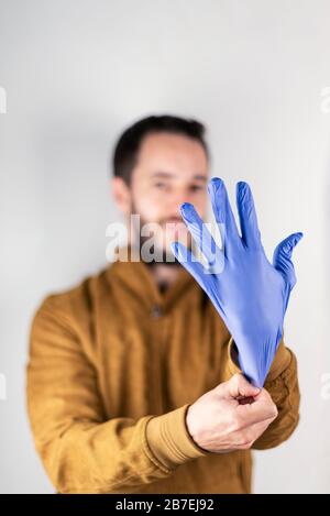 Junger Mann, der einen blauen Latexhandschuh anlegt. Kommerzielles Tonbild mit Schwerpunkt auf der Welt der Reinigung oder Medizin. Stockfoto