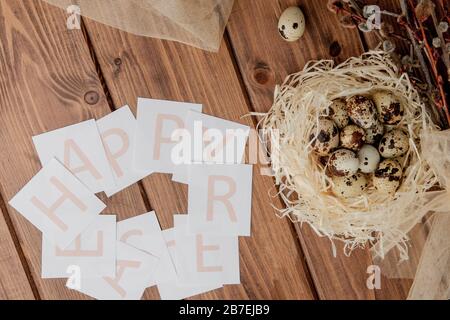 Flache Laienzusammensetzung aus Wachteleiern und Karte mit Text Happy Easter auf Holztisch. Draufsicht. Stockfoto