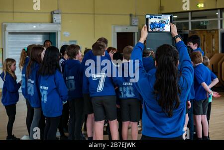 Schulkinder an der Hauptschule Davidsons Mains nehmen an der Übung in der Schulturnhalle Teil, wobei Mädchen Fotos auf dem iPad, Edinburgh, Schottland, Großbritannien machen Stockfoto