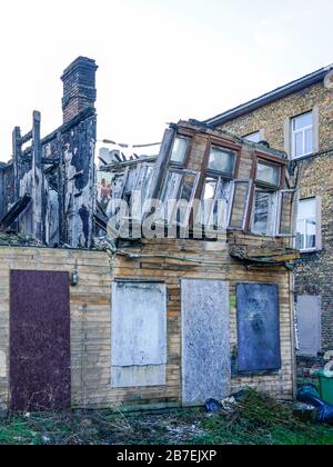Altes Holzhaus nach dem Brand gefährlich eingestürzte Mauer Stockfoto