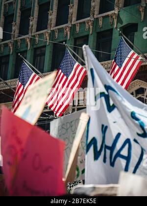 Versammlung von Protestierenden auf der Straße mit Schildern Und drei US-Flaggen im Hintergrund Stockfoto