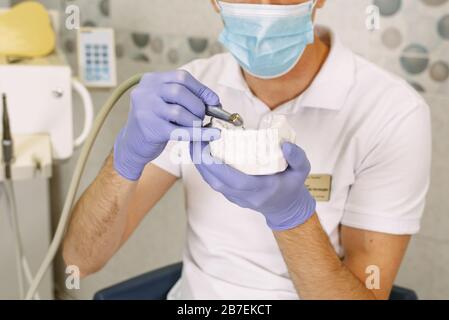 Der Zahnarzt zeigt am künstlichen Kiefer, wie er einen Zahn bohrt und Karies entfernt. Konzentrierter Zahnarzt mit Kieferproben Zahnmodell in der Zahnarztpraxis. Stockfoto