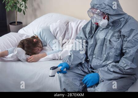 Kranke bewusstlose Frau liegt im Bett, die Augen sind geschlossen. Eine Person, die einen Schutzanzug und eine Maske trägt, sitzt mit dem Kopf nach unten auf dem Bett. Er hält Stockfoto