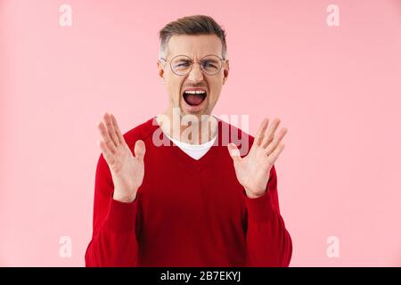 Porträt eines gutaussehenden kaukasischen Mannes, der Brille trägt, die schreit und die Hände über den rosafarbenen Hintergrund hebt Stockfoto