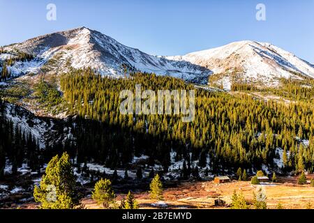 Independence Pass Herbst Sonnenaufgang bei Mining Townsite Buildings in White River National Forest in Colorado mit grünen Kiefern und schneebedeckten Berggipfeln Stockfoto