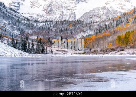 Maroon Bells felsige Berge morgendlicher Sonnenaufgang auf dem See Reflexion in Aspen, Colorado und Herbst gelbes Laub auf Bäumen Waldblick und Winterschnee Stockfoto