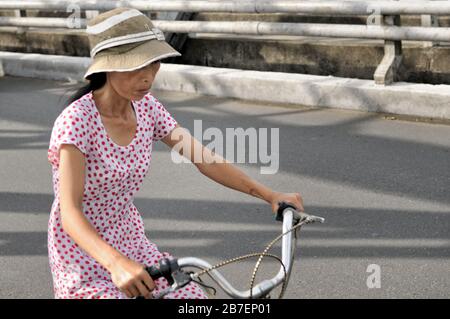 Vietnamesische Frau im Kleid mit dem Fahrrad auf der Trang Tien Brücke in Hue, Vietnam Stockfoto
