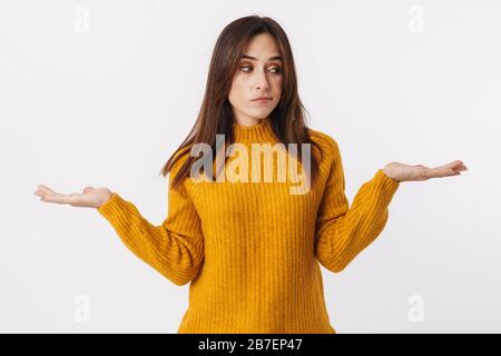 Bild einer schönen brünetten erwachsenen Frau, die einen Pullover mit zögerlicher und über weißem Hintergrund isolierten Händen trägt Stockfoto