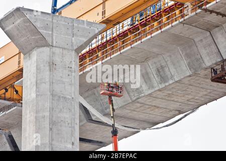 Neue Hafenbrückenkonstruktion, Arbeiter mit verlängertem Kraftheber ausgesetzt, die Zementverbindungen unter der Brücke reinigen. Stockfoto