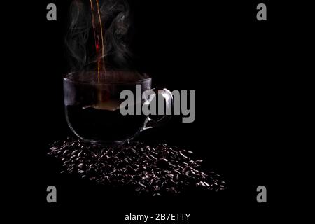 Heißer Kaffee, der auf schwarzem Hintergrund in eine Tasse gegossen wird. Stockfoto