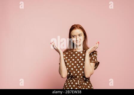 Verwirrte und verrätselte Frau im Studio auf pinkfarbenem Hintergrund. Ein Mädchen in einem schönen braunen Kleid zeigt die Emotionen, nicht zu verstehen. Ich weiß es nicht. Stockfoto