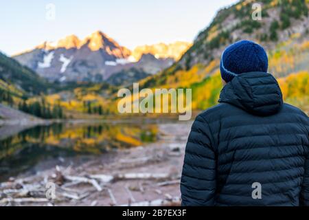 Maroon Bells See bei Sonnenaufgang mit einem Blick auf den Mann in Aspen, Colorado, mit einem felsigen Berggipfel im Oktober 2019 Herbst und lebhaften Bäumen, die auf Wasser reflektiert werden Stockfoto