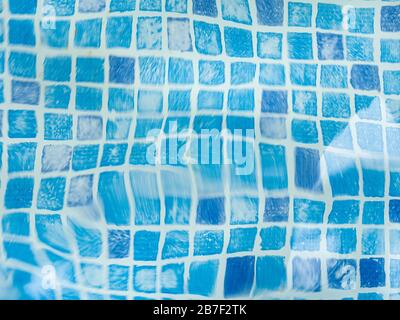 Das Licht, das auf der Oberseite der Wasseroberfläche des Pools reflektiert wurde, war unten mit blauen Mosaikfliesen ausgekleidet. Das Wasser wellt sich auf der Rückseite des blau gefliesten Schwimmbads Stockfoto