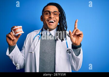 Der junge afro-amerikanische Zahnarztarzt, der Stethoskop mit Zähnen trägt, überraschte mit einer Idee oder Frage, mit dem Zeigefinger mit einem glücklichen Gesicht zu zeigen, n Stockfoto