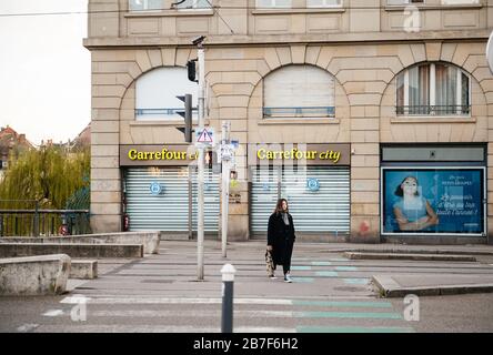 Straßburg, Frankreich - 15. März 2020: Junges Mädchen, das die Straße vor dem Carrefour City Supermarkt durchquert, während Frankreich mit einem Ausbruch des Coronavirus COVID-19 grappt Stockfoto
