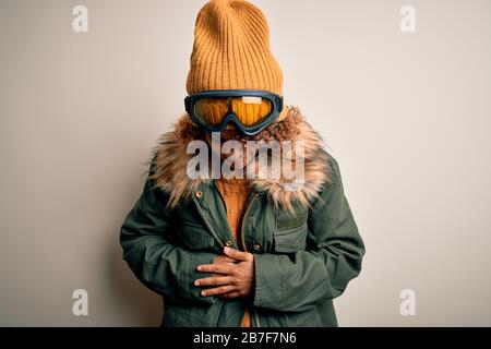Junge afroamerikanische Skifahrerin mit lockigen Haaren, die Schneesportkleidung trägt und eine Skibrille mit Hand auf dem Bauch, weil Verdauungsbeschwerden, schmerzhafte Krankheit f Stockfoto