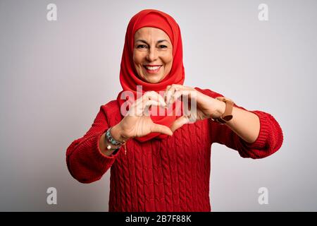 Frau aus der mittleren Zeit, die einen traditionellen muslimischen Hijab über einem isolierten weißen Hintergrund trägt, lächelt in Liebe und macht Herzsymbole mit den Händen. Romanti Stockfoto