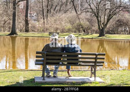 Auf einer Parkbank sitzend, genießt das ältere Paar im Frühjahr einen warmen Tag. Stockfoto