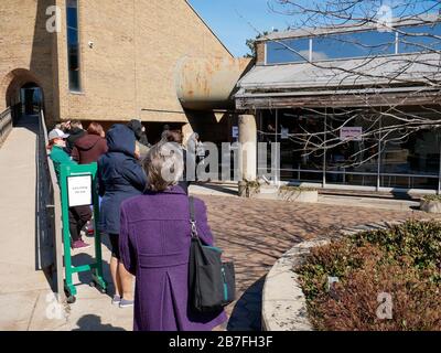 Oak Park, Illinois, USA. März 2020. Die frühen Wähler für die Wahl der Illinois Primary am Dienstag wurden getroffen, um sich heute außerhalb der Village Hall zusammenzuschließen, um zu vermeiden, dass sie im Gebäude zusammengedrängt werden. Auch Schulen und Bibliotheken sind bis zum 31. März geschlossen, um Coronavirus/COVID-19 von der Verbreitung fernzuhalten. Stockfoto