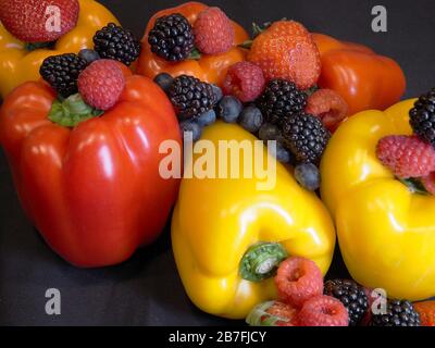 Orange Rot Gelb Bell Peppers mit einer Auswahl an Beeren, die um sie herum angeordnet sind Stockfoto