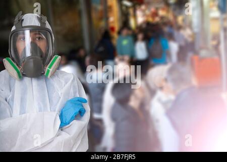 Arbeiterinnen tragen Schutzanzug und Gasmaske mit Hintergrundfoto von vielen Menschen in der Gemeinde. Stockfoto