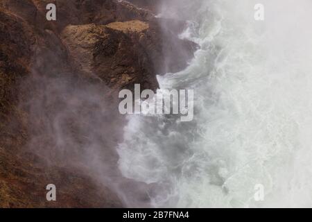 Wenn Sie auf die Basis der Lower Falls im Yellowstone River hinunterblicken, interagieren Wellen und Nebel mit den Felswänden des Canyons im Yellowstone National Stockfoto