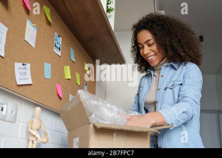 Lächelnde afrikanische Mädchenkunde öffnet Paketbox zu Hause. Stockfoto